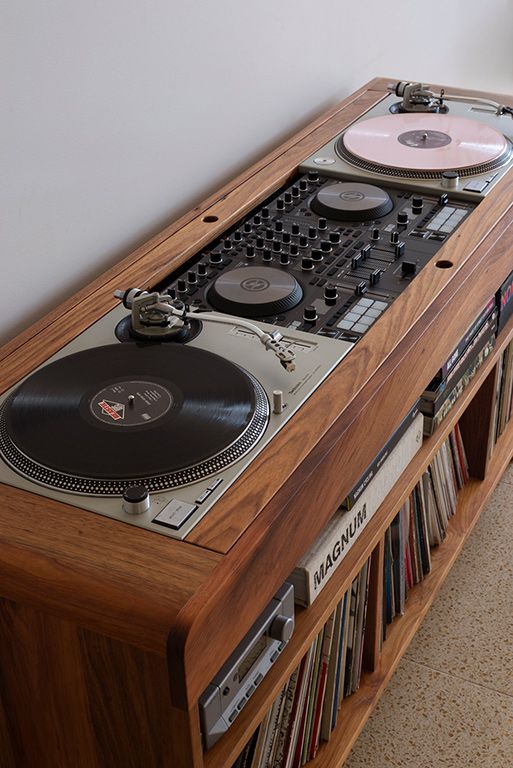 Vintage DJ equipment setup with dual turntables and mixer, housed in a wooden cabinet with a collection of vinyl records.