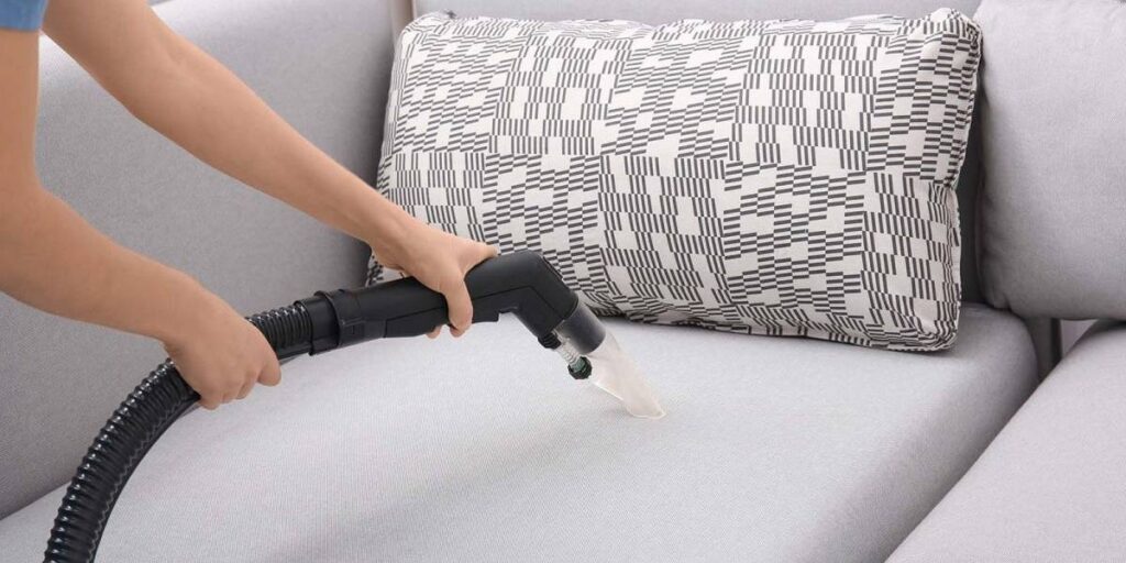 Vacuuming a gray sofa with a handheld cleaner, removing dust and debris for a fresh and clean look.