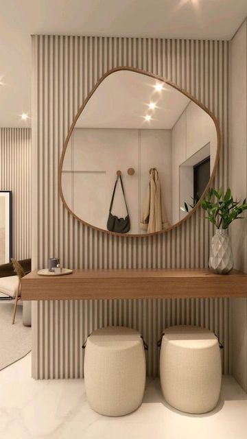 Modern minimalistic hallway with abstract mirror, wooden console, poufs, and potted plant on striped wall.