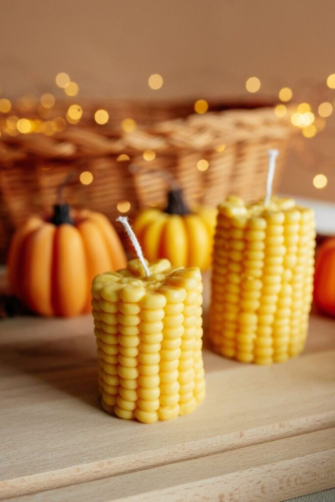 Festive corn-shaped candles with pumpkins and fairy lights create a cozy autumn ambiance on a wooden surface.