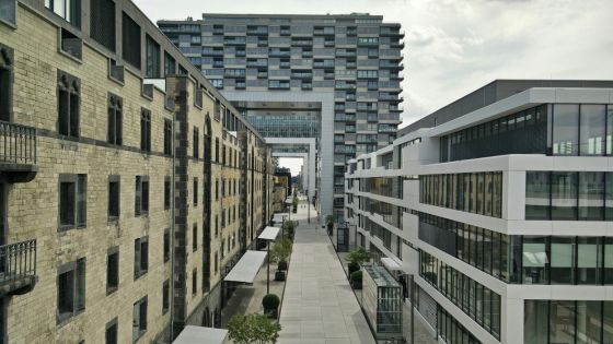 Modern and historic buildings face each other along a walkway leading to a contemporary high-rise in an urban cityscape.