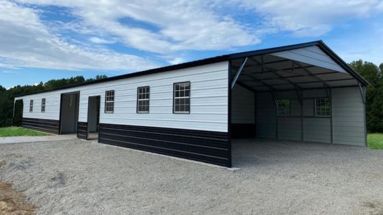 Large metal storage building with garage and multiple windows, set on gravel with trees and blue sky in the background.