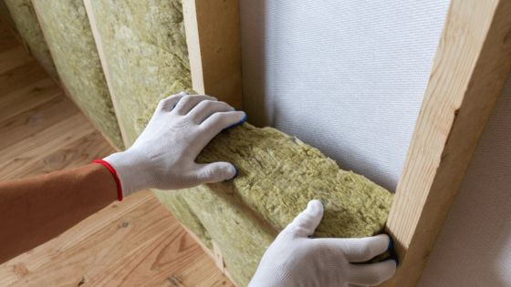 Worker installing mineral wool insulation in wall frame, enhancing energy efficiency and soundproofing in building.