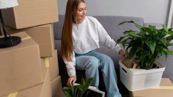 Woman unpacking boxes with houseplants in living room on moving day.