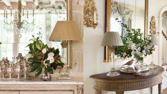 Elegant living room decor with floral arrangements, vintage mirrors, and silver accents under warm lighting.