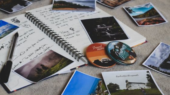 Open travel journal with photos and travel-themed pins on a table.