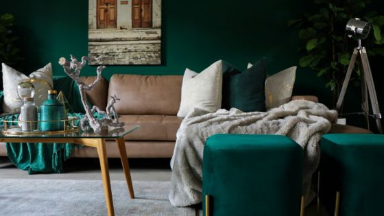 Stylish living room with beige sofa, green accents, and modern decor in front of a dark green accent wall.