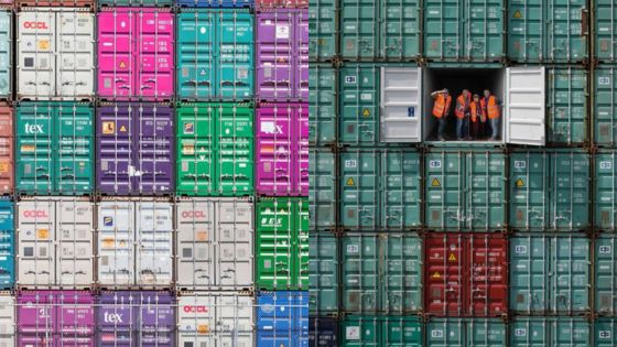 Stacked colorful shipping containers with open door revealing workers in safety vests, symbolizing global trade and logistics.