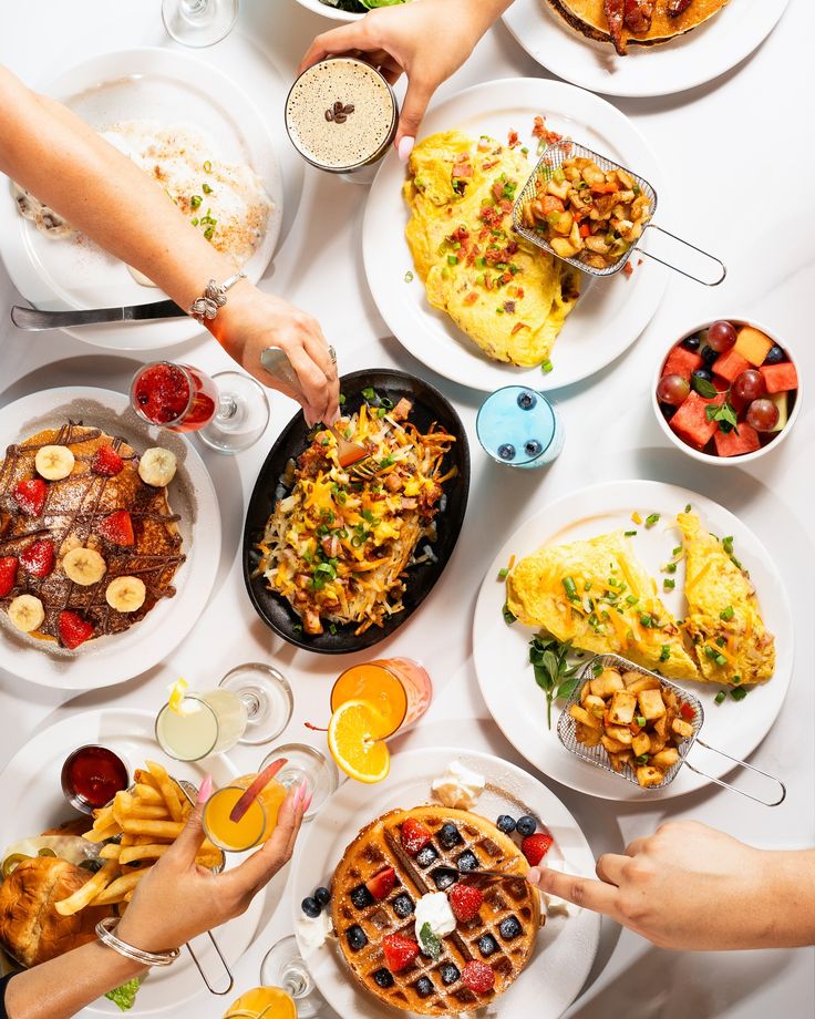 A vibrant brunch spread with waffles, omelets, fresh fruit, coffee, and juice on a white table.