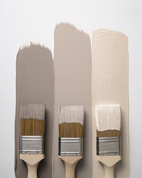 Three brushes with taupe paint strokes on a white wall, showcasing neutral color palette options for interior design.