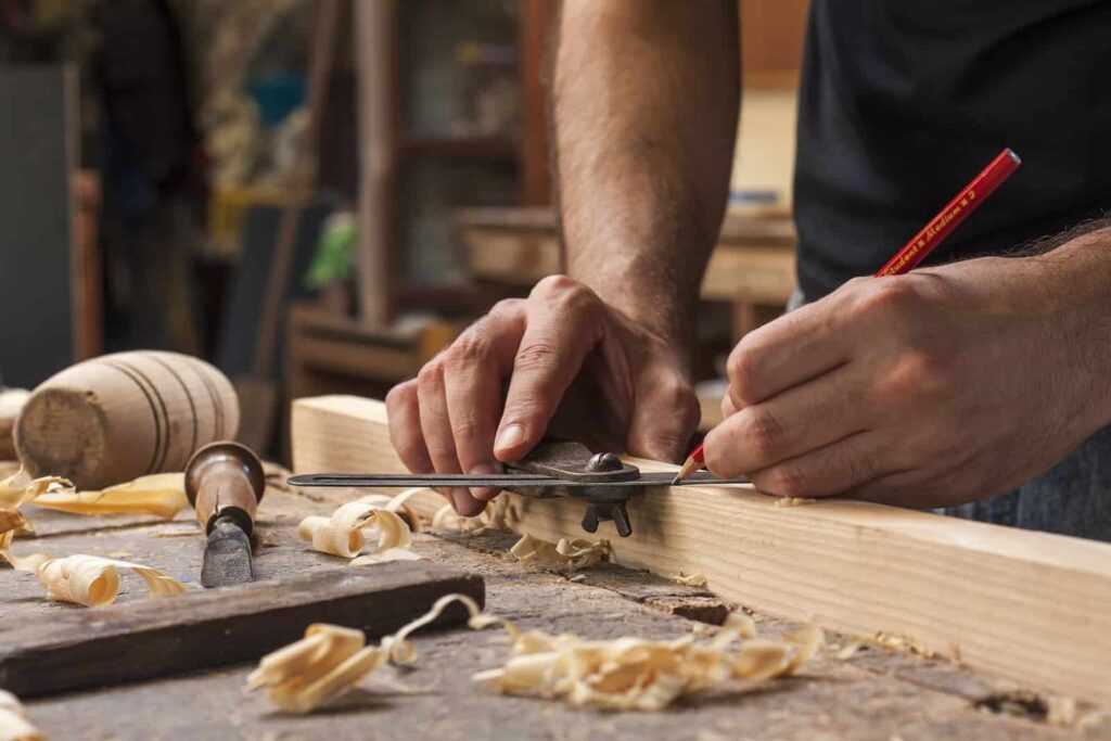 Woodworker marking lumber with precision in a workshop, surrounded by tools and wood shavings.