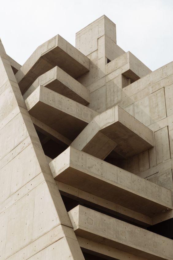 Brutalist concrete architecture with geometric design and angular protrusions against a cloudy sky.