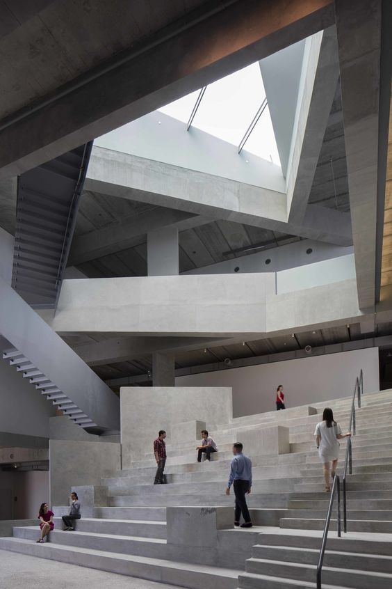 Modern architectural space with concrete steps and people interacting, featuring geometric design and natural light.