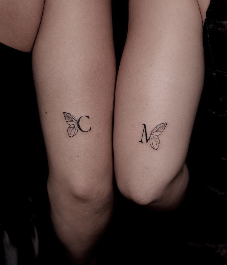 Minimalist butterfly wing tattoos with initials on two arms.