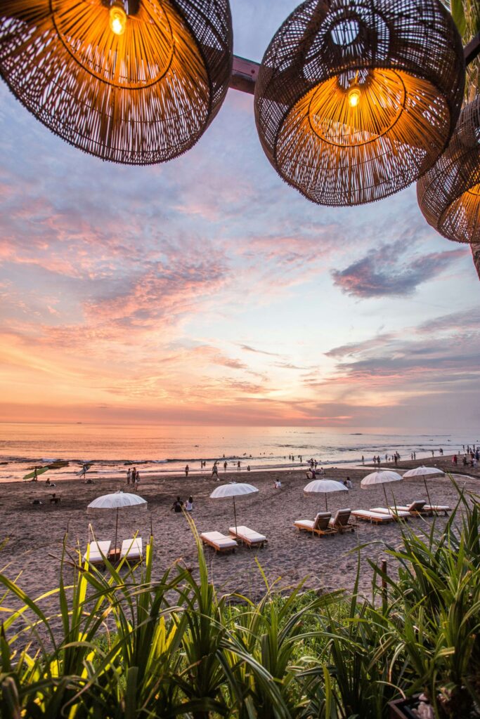 Beach sunset with lounge chairs and parasols under warm woven lamps, capturing evening relaxation vibes.