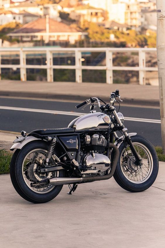 Classic silver motorcycle parked by the road with urban backdrop and sunset lighting.