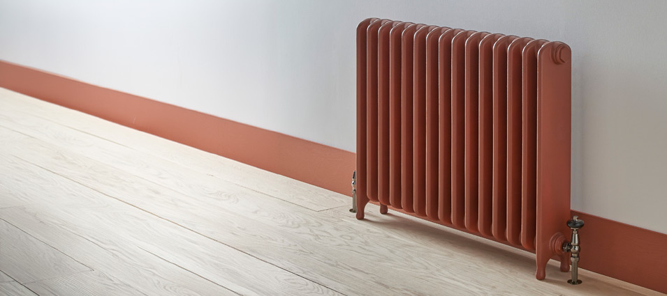 Red radiator against white and orange wall on light wood floor, classic home heating design.