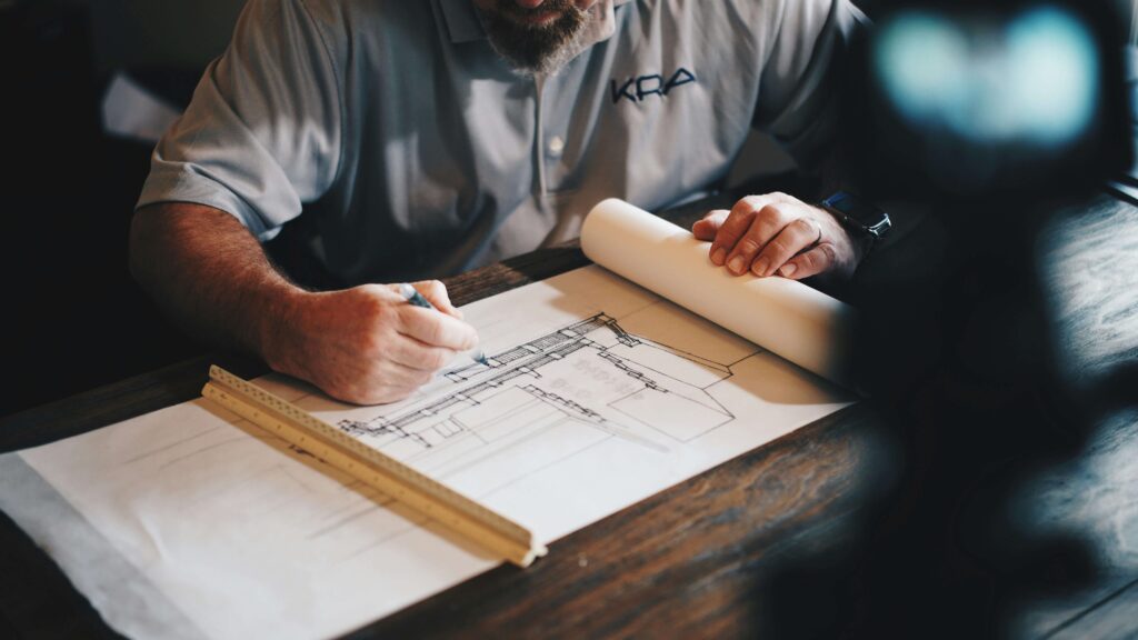 Architect drawing blueprints at desk with ruler, highlighting design process and construction planning.