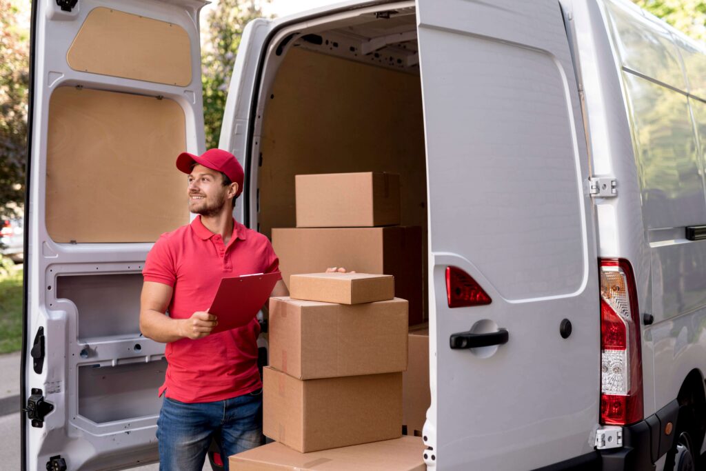 Delivery person with clipboard unloading boxes from a van in a sunny outdoor setting.