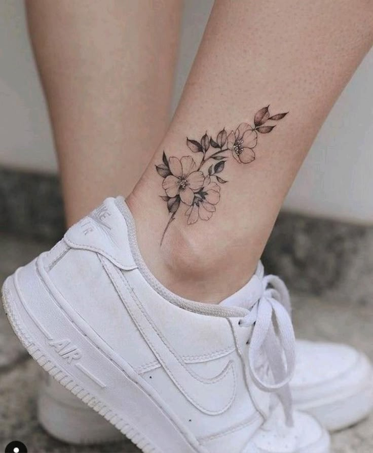 Delicate floral ankle tattoo with white sneakers, showcasing elegant leg art and casual footwear style.