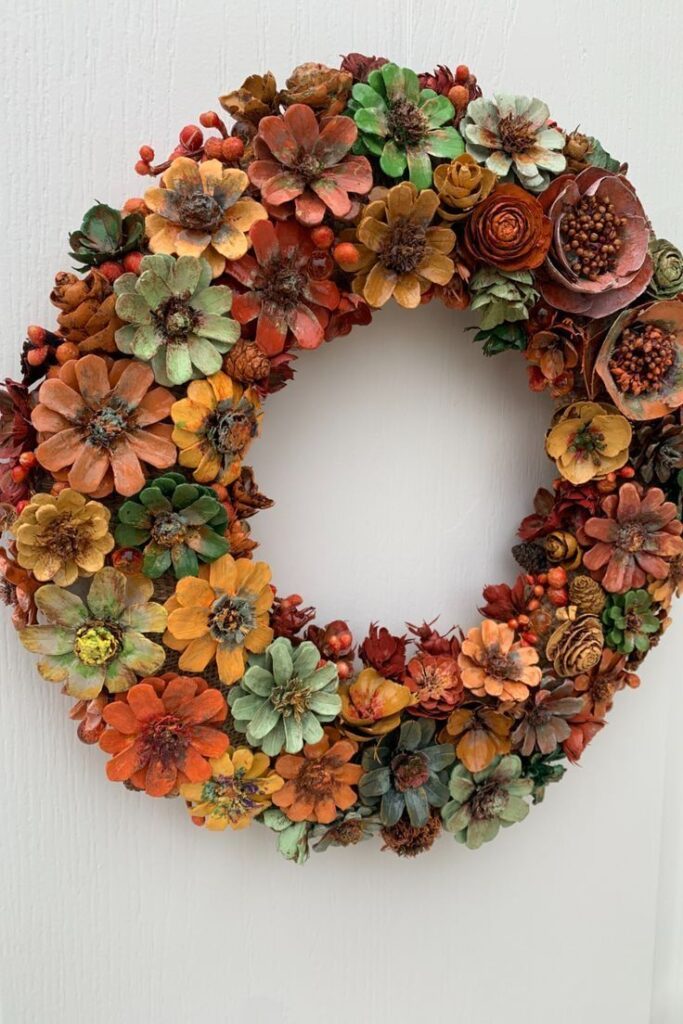 Vibrant autumn wreath made of pinecones and flowers against white background, showcasing fall colors and textures.