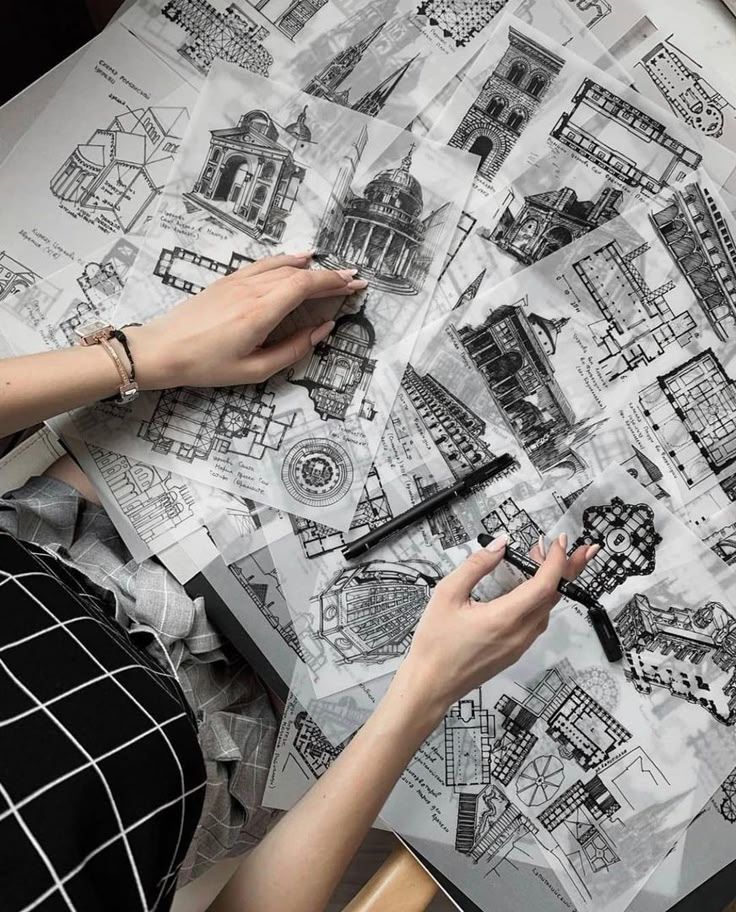 Hands arranging architectural sketches and plans on a desk, showcasing detailed drawings and designs.