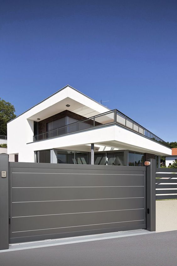 Modern minimalist house with large windows and a sleek metal gate under a clear blue sky.