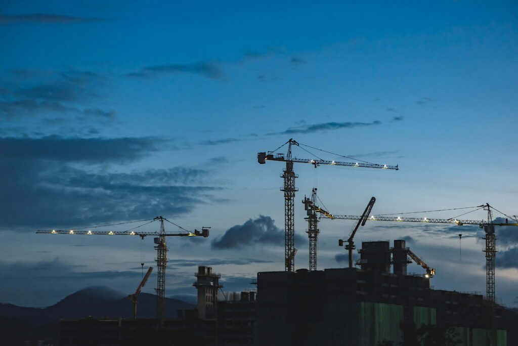 Construction site with cranes silhouetted against a blue evening sky.