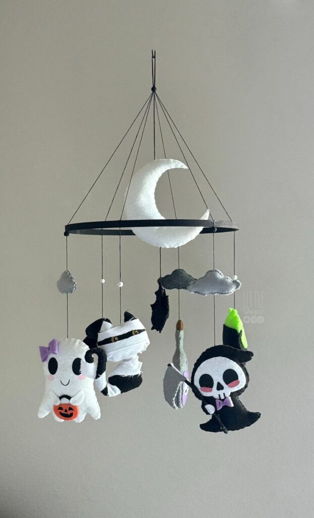 Halloween mobile with felt ghost, mummy, and reaper hanging from crescent moon. Cute spooky decor.