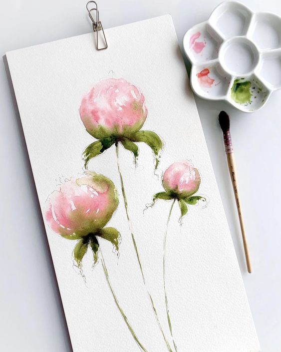 Watercolor painting of pink peonies with green leaves, next to a paintbrush and palette on a white surface.