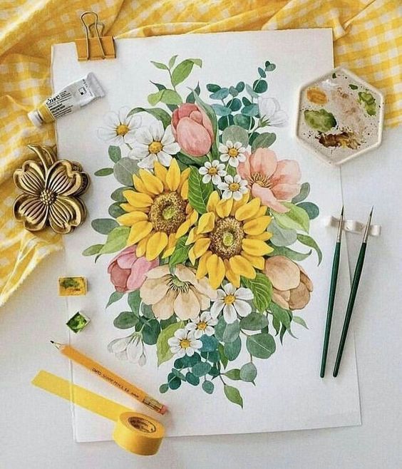 Colorful watercolor painting of sunflowers, tulips, and daisies, surrounded by art supplies on a white and yellow checkered table.