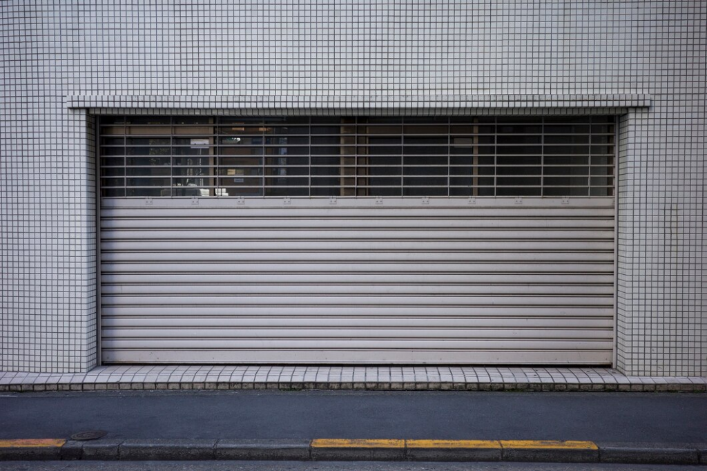 Closed garage door with metal grille in a tiled building facade. Urban architecture detail.