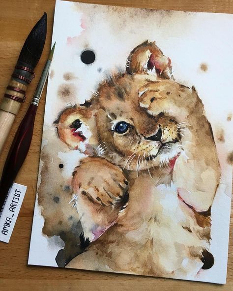 Watercolor painting of a playful lion cub on paper with brushes nearby, by artist Anna.