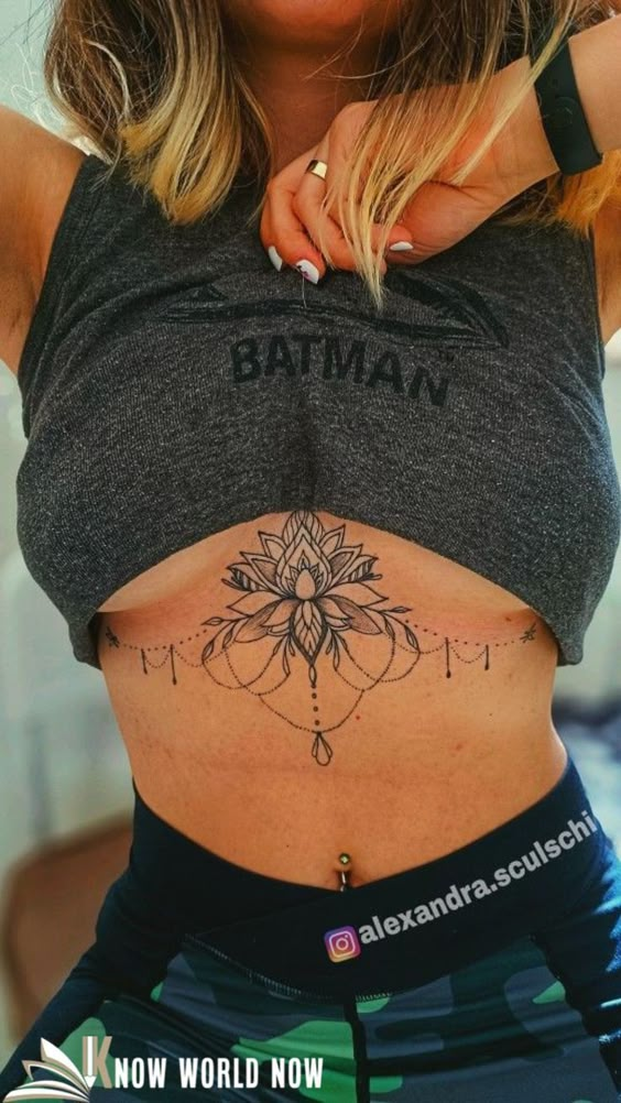 Woman showing intricate floral underboob tattoo, wearing a Batman crop top and camo leggings.