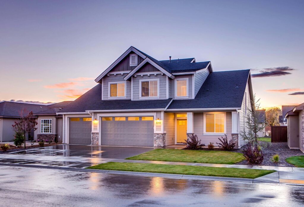 Modern two-story house with a well-lit exterior, three-car garage, and manicured lawn at sunset.