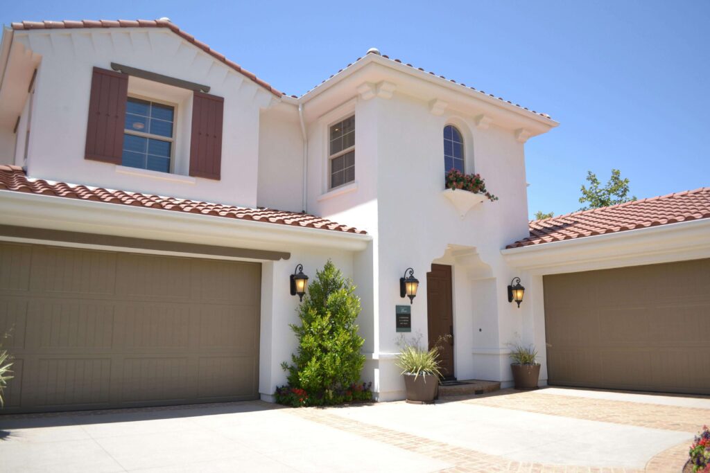 Modern Mediterranean-style white house with terracotta roof, double garage, and landscaped entryway.