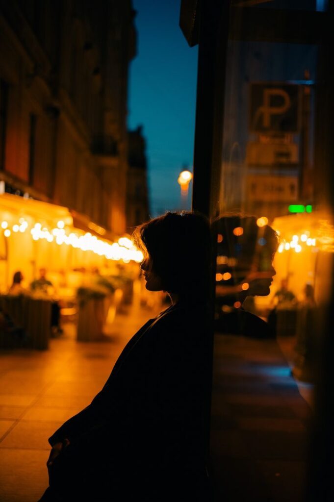 Silhouette of a person in a dimly lit city scene, with warm glowing lights and reflections at night.