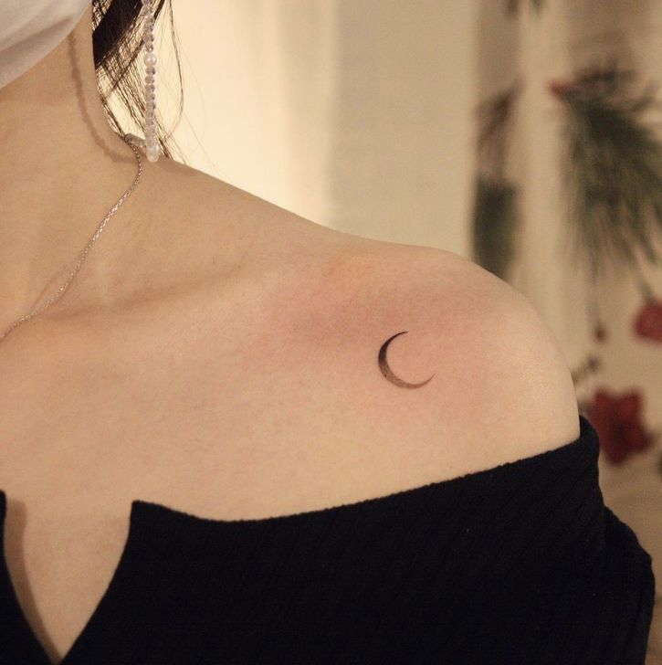 Crescent moon tattoo on bare shoulder in soft lighting, elegant and minimalistic design.