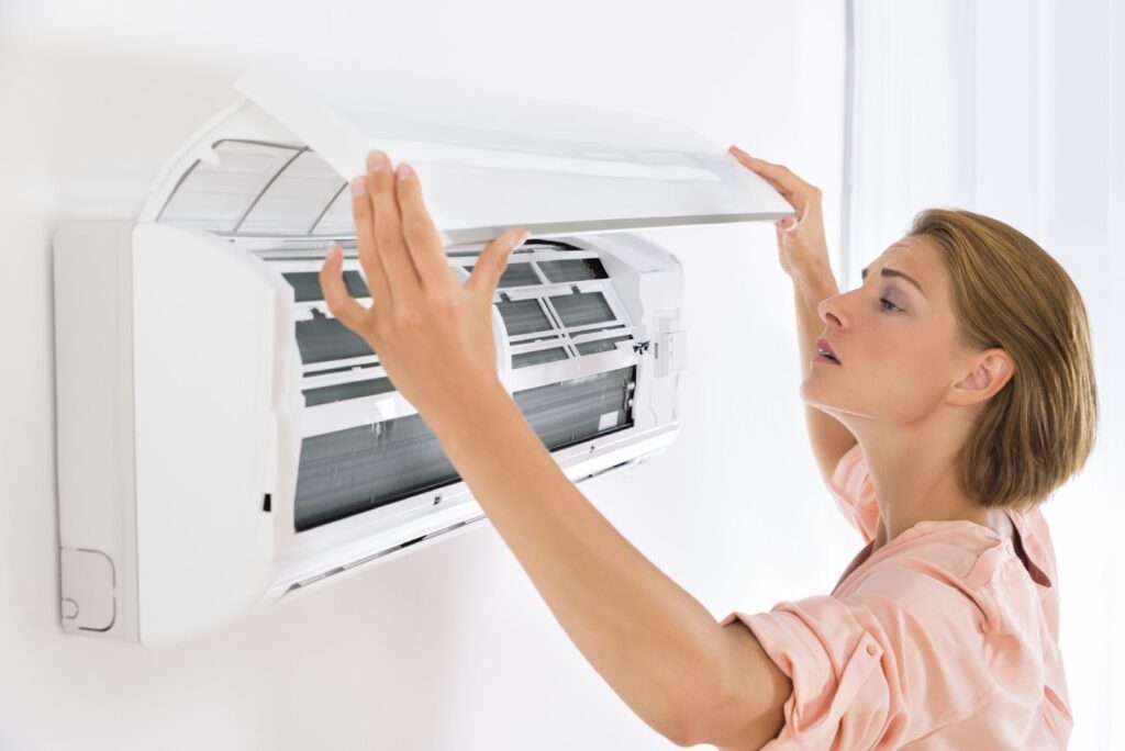 Woman inspecting and opening the cover of a wall-mounted air conditioner at home.