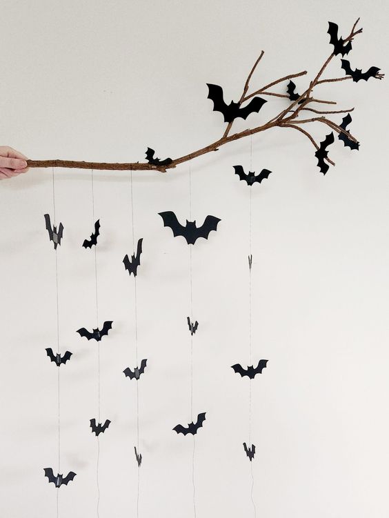 DIY Halloween decoration with hanging black paper bats on a branch.