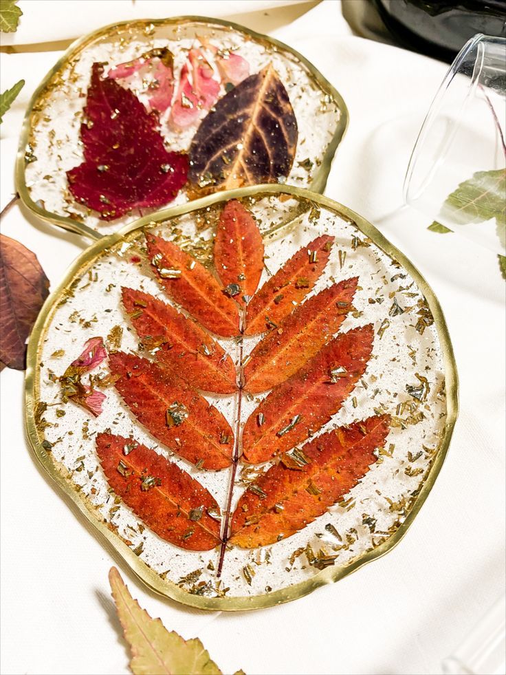 Handmade resin coasters with preserved autumn leaves and gold accents on a white cloth background.