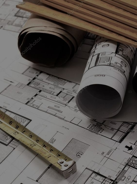 Architectural blueprints with measuring tape and rolled plans on a desk, representing construction and design.