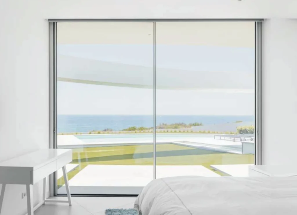 Modern bedroom with ocean view through large glass doors, showcasing minimalist design and natural light.