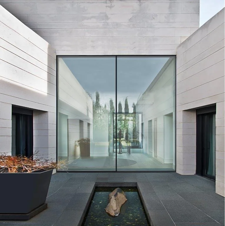 Modern house courtyard with large glass window and minimalist design, featuring a small rectangular pond with a rock.