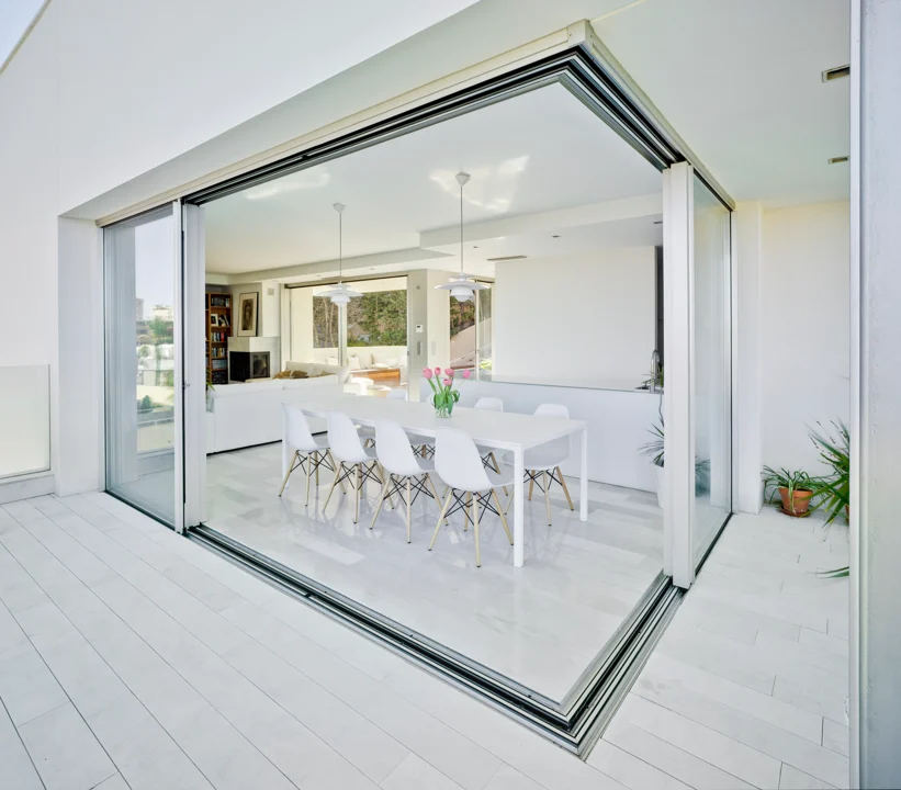 Modern open-plan dining room with glass walls, white decor, and natural light. Contemporary minimalist interior design.