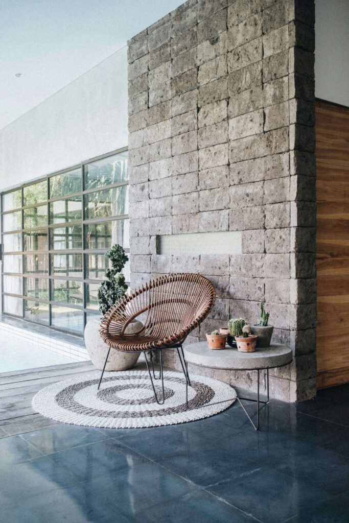 Cozy modern patio with wicker chair, stone wall, and plants, creating a relaxing outdoor space.