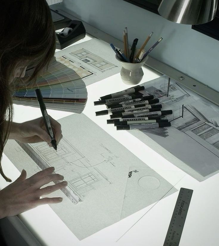 Architect drawing with markers and rulers on a lightbox, detailed draft and design tools visible.