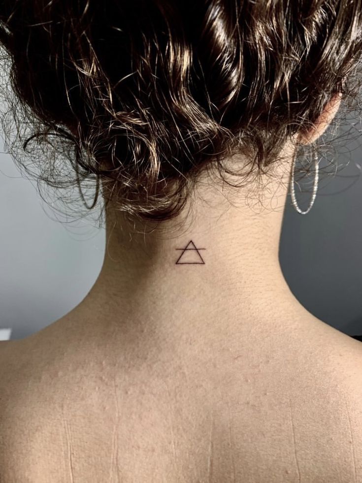 Minimalist triangle tattoo on the nape of a person's neck with curly hair.