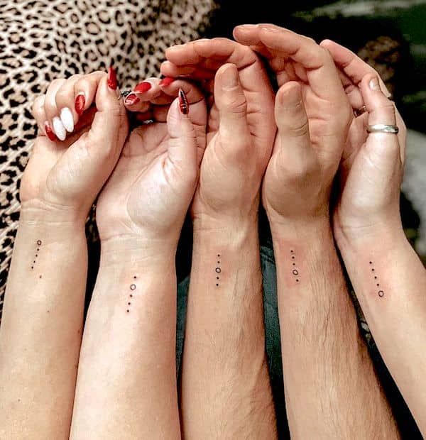 Four forearms with minimalist dot and line tattoos, showcasing friendship or family matching designs.