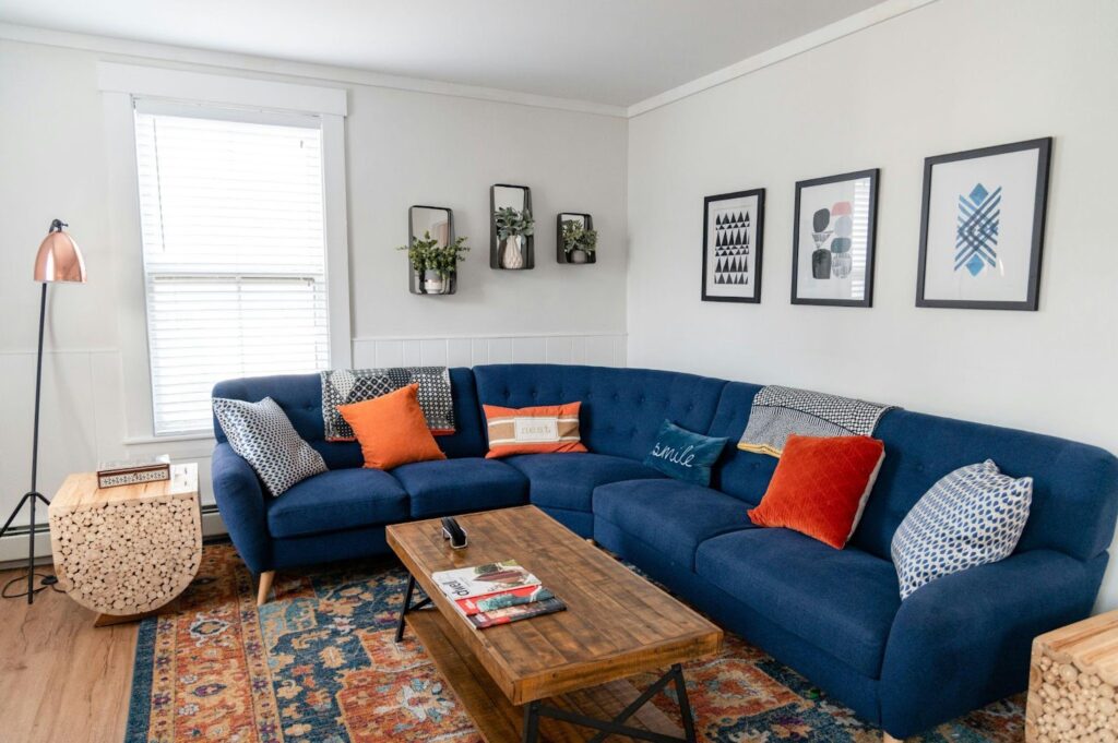 Cozy living room with blue sectional sofa, colorful pillows, wooden table, and wall art for modern interior design.